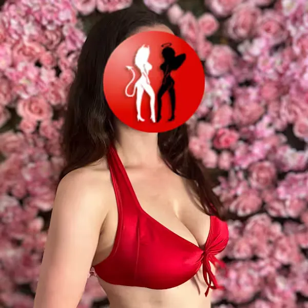 Annabell in rotem Dessous vor rosafarbener Blumenwand – ihr sinnlicher Blick und ihr üppiges Dekolleté wirken wie ein erotisches Versprechen.