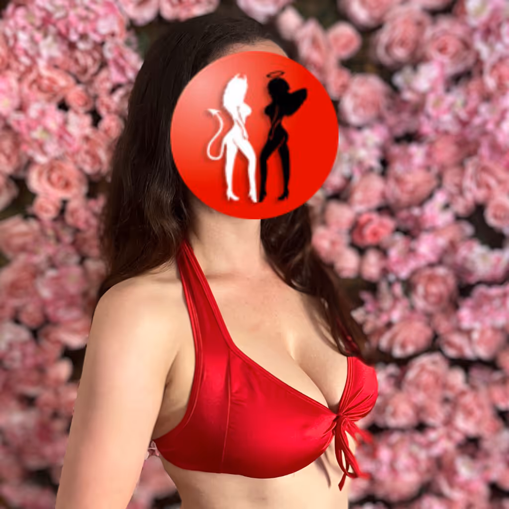 Annabell in rotem Dessous vor rosafarbener Blumenwand – ihr sinnlicher Blick und ihr üppiges Dekolleté wirken wie ein erotisches Versprechen.