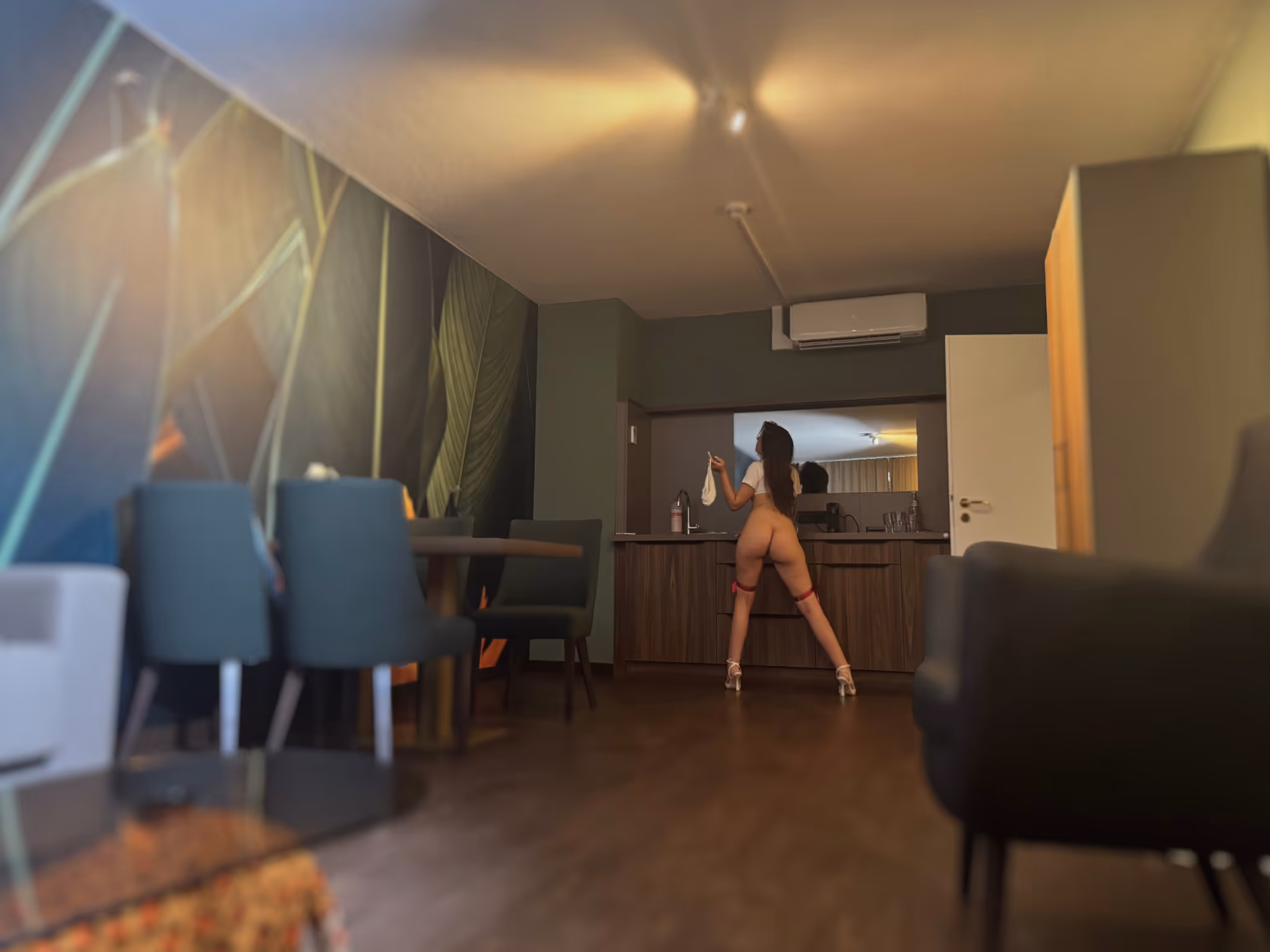 Mila steht nackt in High Heels mit dem Rücken zur Kamera an einer Küchenzeile. Ihr schlanker Körper und die langen Beine kommen im Kontrast zum modernen Raum besonders sinnlich zur Geltung.