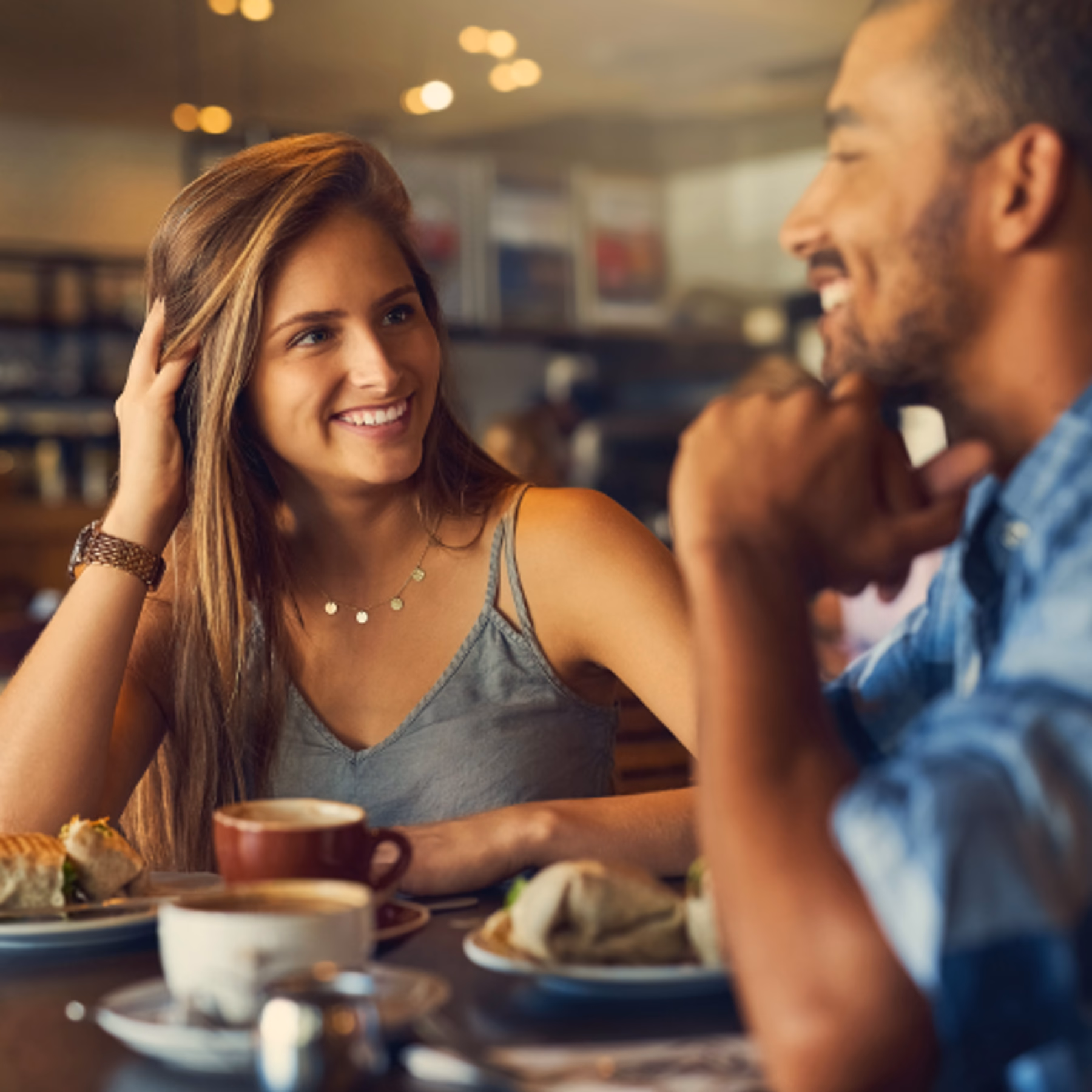 Gezeigt wird eine Situation, bei dem sich eine Frau und ein Mann daten. Die Frau lächelt den Mann zufrieden an und ist sichtbar an dem interessiert, was er über sich erzählt.