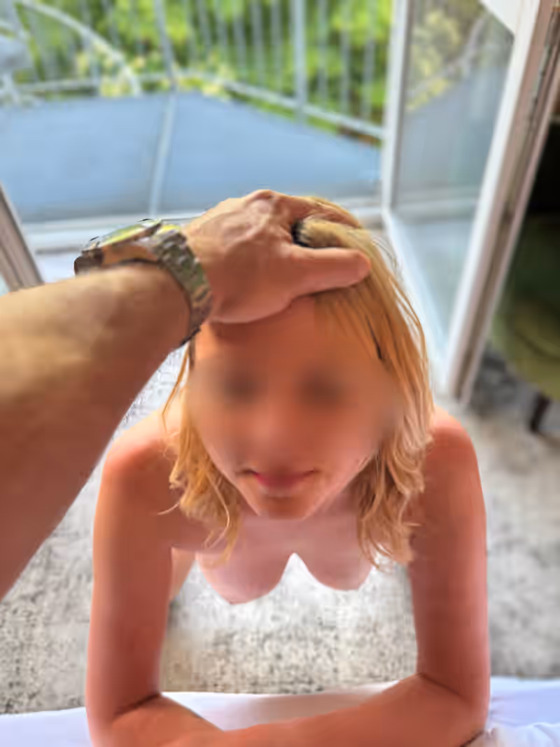 Escort Matilda kniet nackt auf dem Bett, dein Griff in ihrem Haar. Ihr Blick nach oben ist unterwürfig – bereit, dich mit Hingabe zu verwöhnen. Pure Kontrolle. Pure Lust.