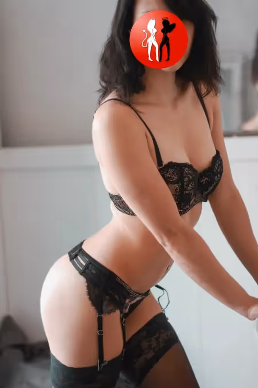 Lucy kniet elegant auf dem Bett, ihr Rücken leicht gedreht, sodass der schwarze Spitzenbody ihre schlanke Silhouette betont. Die kunstvoll gestalteten Rückenträger und das verspielte Cut-Out-Design geben dem Look eine aufregende Tiefe. Mit schwarzen High Heels ergänzt sie ihr Erscheinungsbild um eine Prise dominanter Sinnlichkeit. Die Szene ist weich ausgeleuchtet, was ihre feminine Aura sanft unterstreicht.

