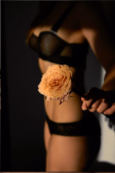 Eine Frau in schwarzer Unterwäsche von der Seite fotografiert, sie hält eine Blüte in ihrer Hand